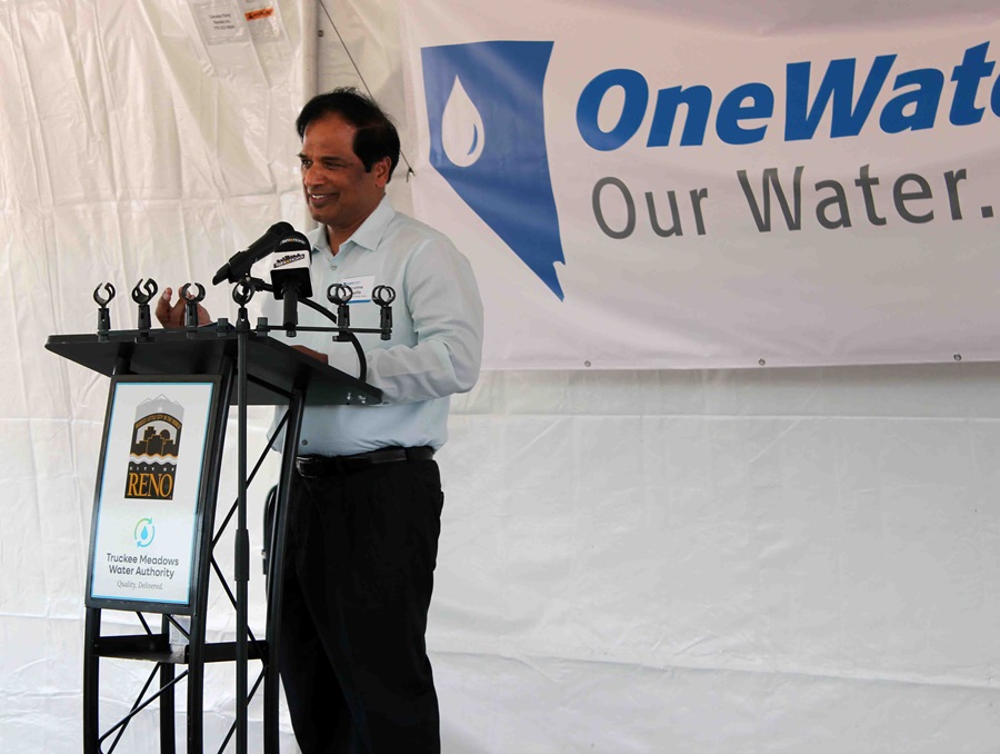 Krishna Pagilla speaking at a podium with a sign that reads "City of Reno" and "Truckee Meadows Water Authority," behind him a banner that reads "One Water. Our Water."