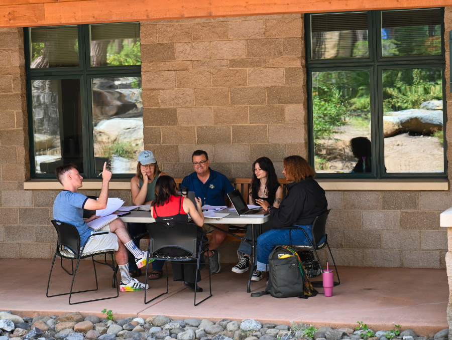 A group of people sitting at a table outside, talking and working, on campus at Lake Tahoe.