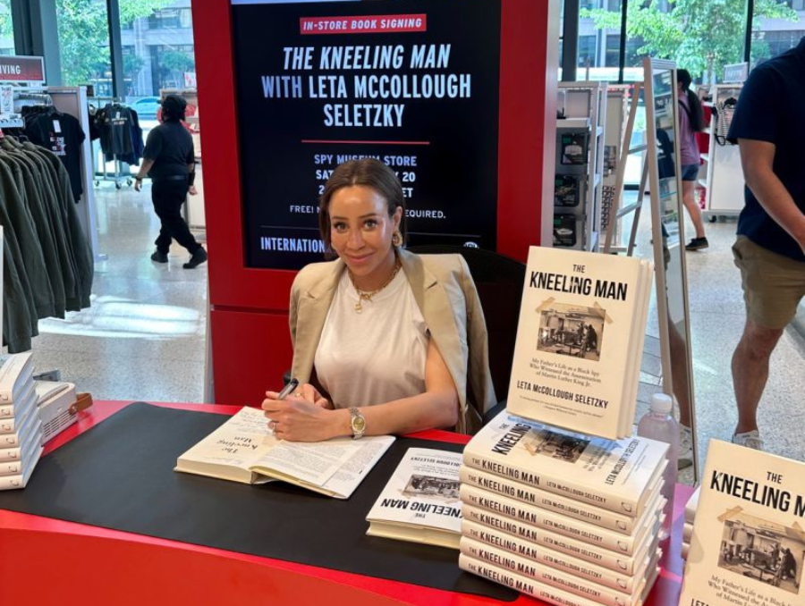 Leta smiling at a table with tens of copies of her book.