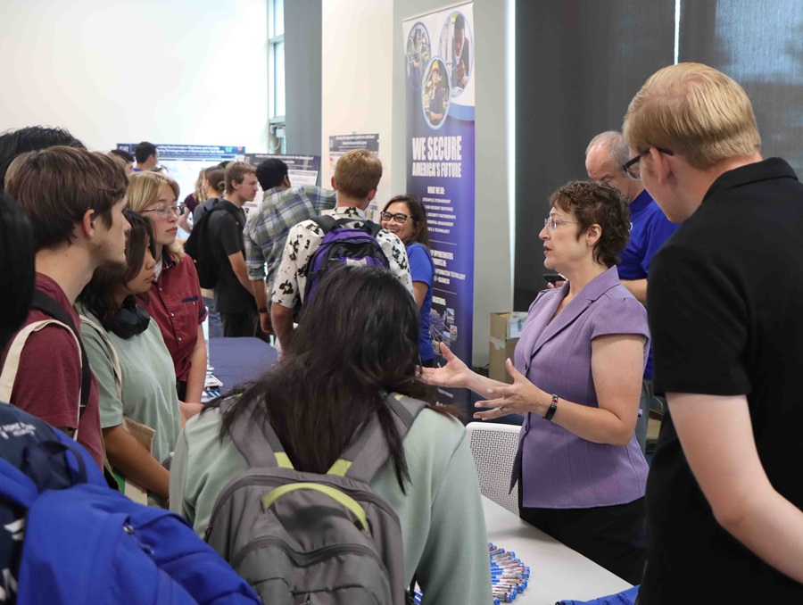 A person at a booth speaking with students and attendees at the Nuclear Career Spotlight event.