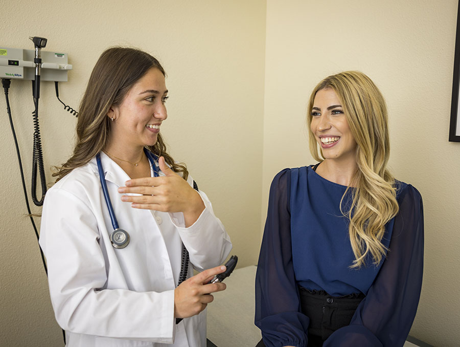 A PA student in a white coat talking with a patient in a clinical setting.