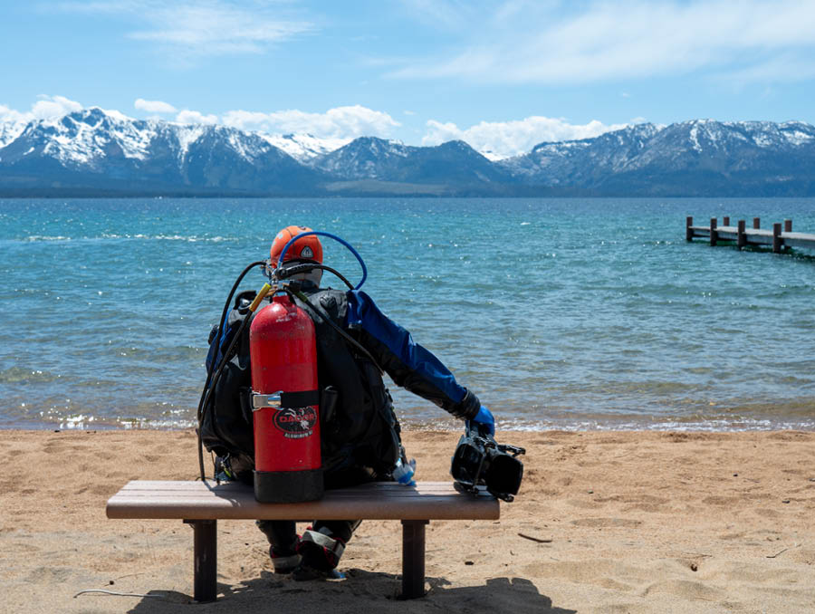 Emily Carlson sits on a bench on a Tahoe beach in her scuba gear.