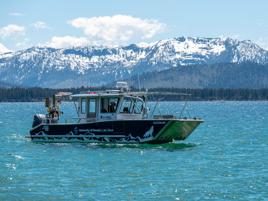 The R/V Liberty vessel floating on Lake Tahoe with snowy mountains in the background.