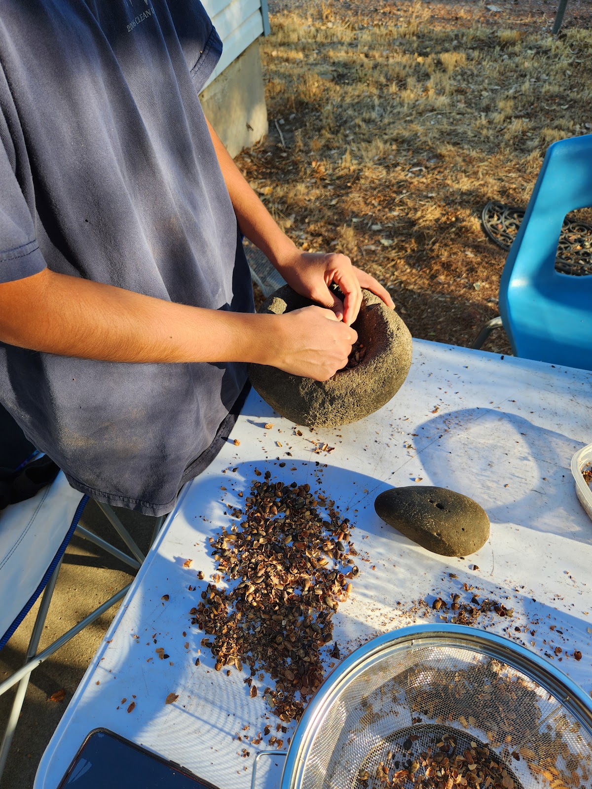 Someone's hands working near a stone bowl, grinding up ingredients on an outdoor table.