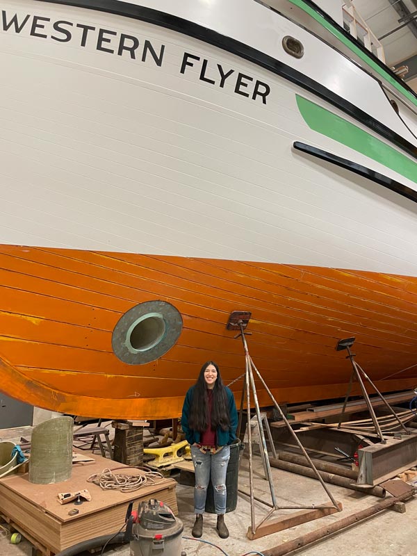 Alejandra poses next to a large ship called the Western Flyer
