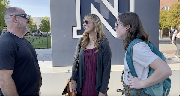 Three students stand in front of the N statue on campus speaking to one another.