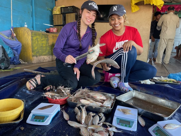 Two student researchers smiling at the camera with fish in their hands wearing Nevada hats.