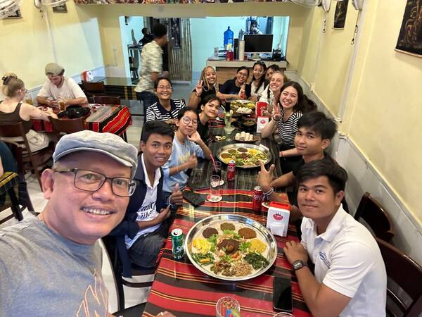 A large group of people at a long table eating dinner and smiling up at the camera.