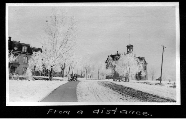 A historical image in black and white showing snow-covered trees and grass leading to Morrill Hall with a walkway shoveled from 1911.