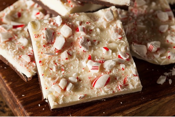 Two square pieces of peppermint bark dessert piled on top of one another on a wooden table.