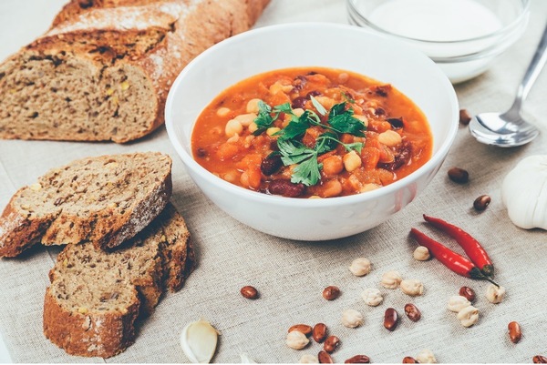 Two slices of brown bread placed next to a bowl of vegan white bean chili on a table.