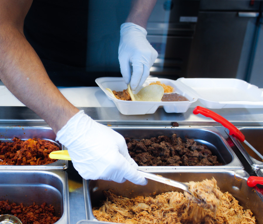 A man's arms as he serves tacos, scooping up ingredients.