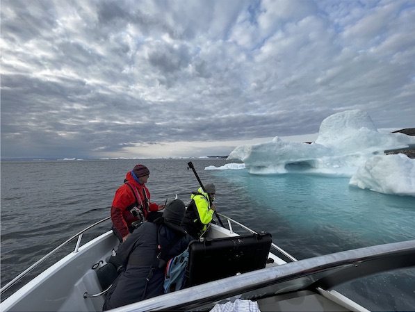 People on a boat wearing coats and floating near a big glacier.