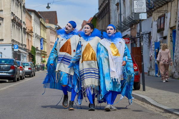 Three people in costume and clown makeup pose in the center of a street during a performance.