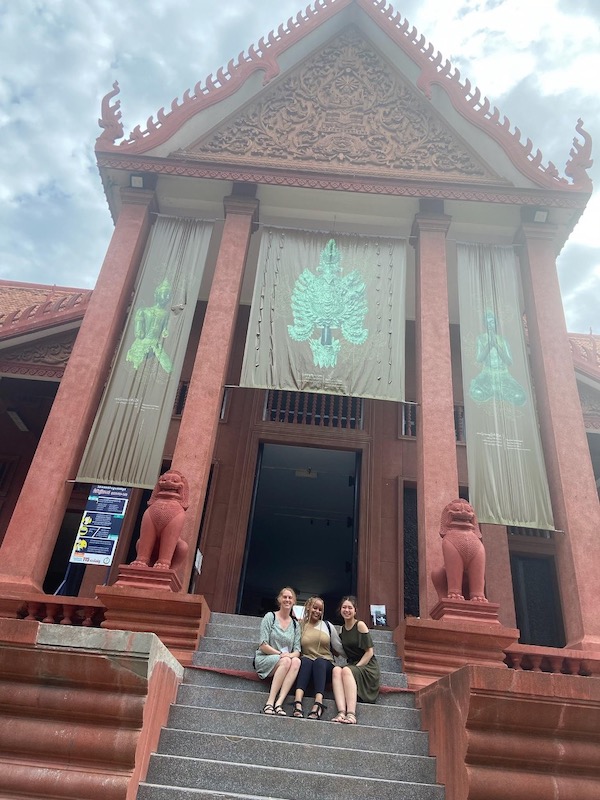 Three women sit on the steps of an ornately carved temple.