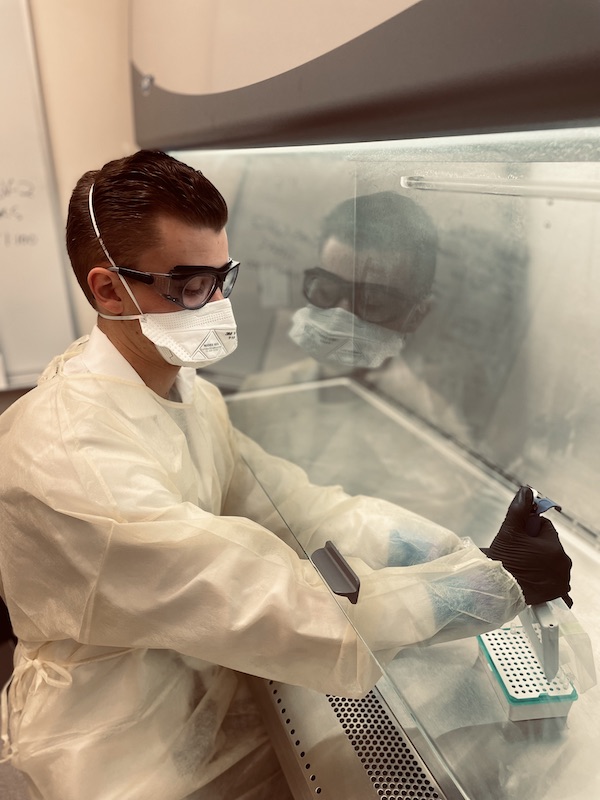 Gillis wearing a mask, gloves, and eye protection in a lab working with samples.