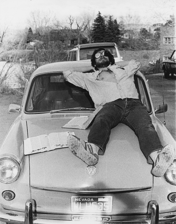 A student lays down on the hood of a car. 