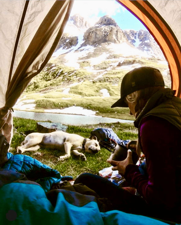 A woman sits in a tent with a dog laying down next to her.