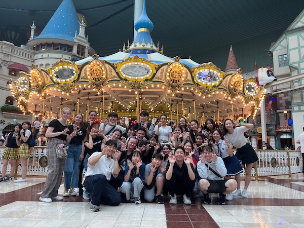 A large group of students posing with their hands raised like paws in front of a big ornate carousel.