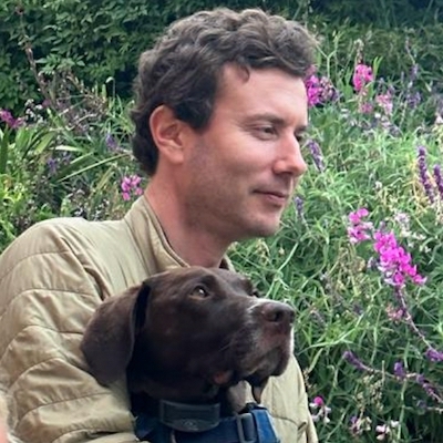 Sean McCain outside with a dog looking off into the distance in front of flower bushes.