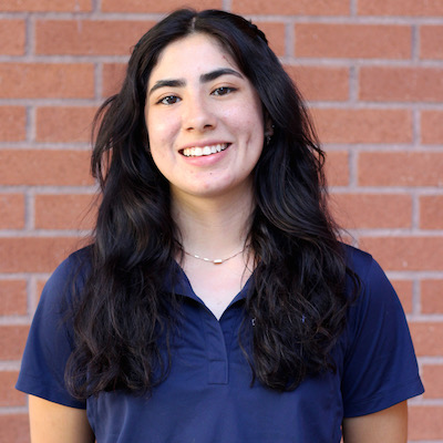 Paoloa Miramontes Gonzales smiling for a headshot against a brick wall.