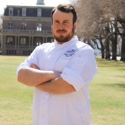 Matt stands with arms crossed in a chef jacket on the University's quad.