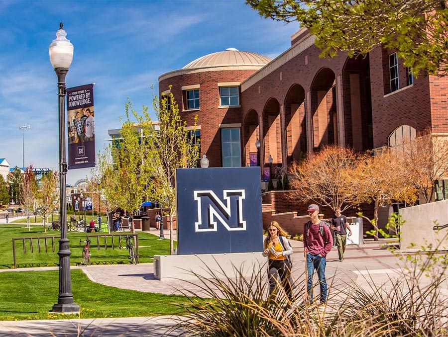 Two University of Nevada, Reno students walking down the walkway in front of the Mathewson-IGT Knowledge Center and Block N statue