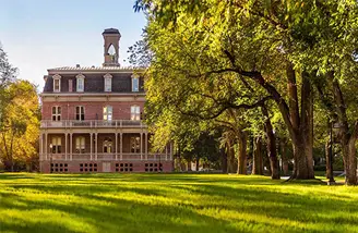 A view looking south on Morrill Hall on the University of Nevada, Reno, an old brick building with a bell tower, surrounded by trees and the green grass of the University quad.