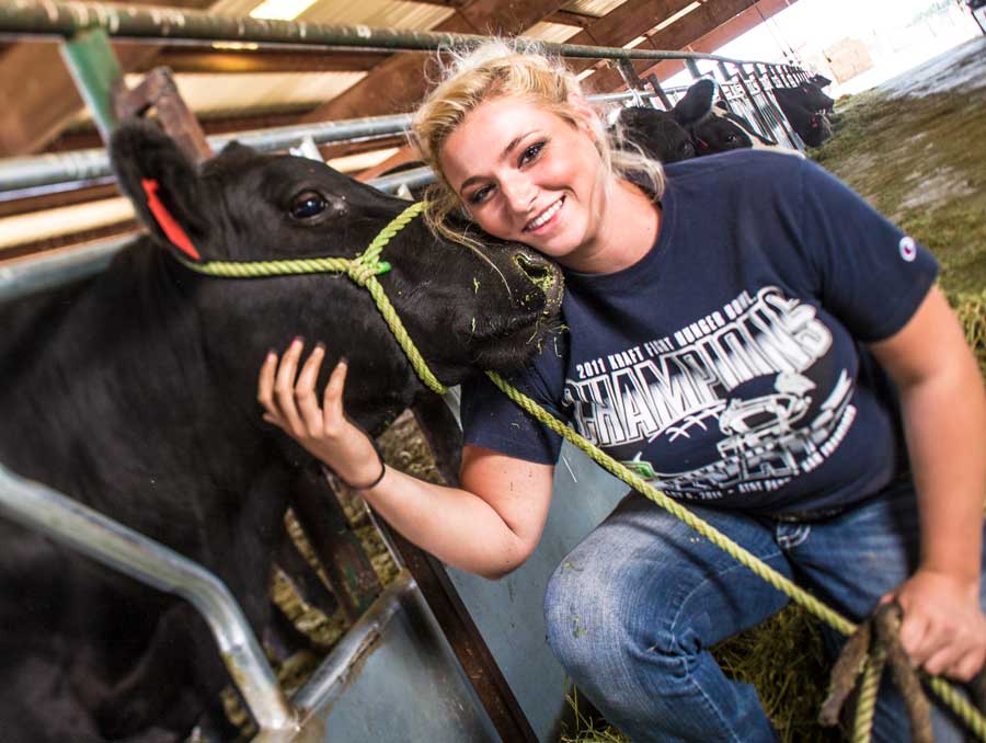 A student leans in close to a cow in a pen and presses her face against the cows nose