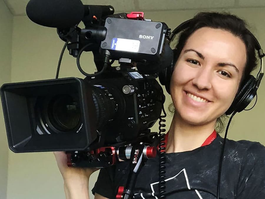 A student holding a TV camera, wearing a headset and smiling.