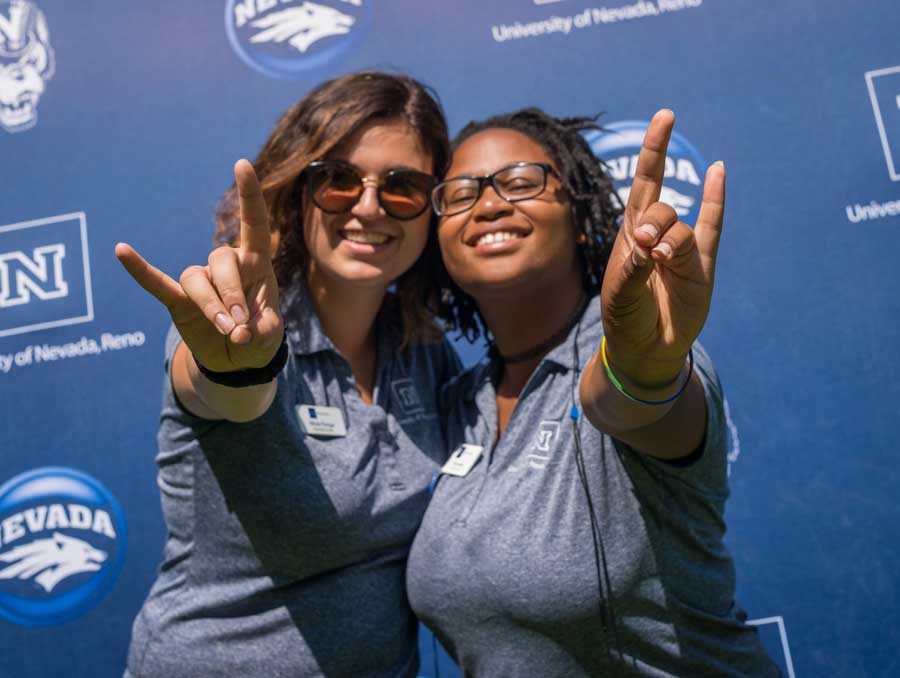 Two orientation leaders make the Wolf sign for the camera