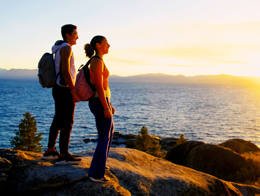 Two students on a lakeshore with the sun rising across the opposite shore