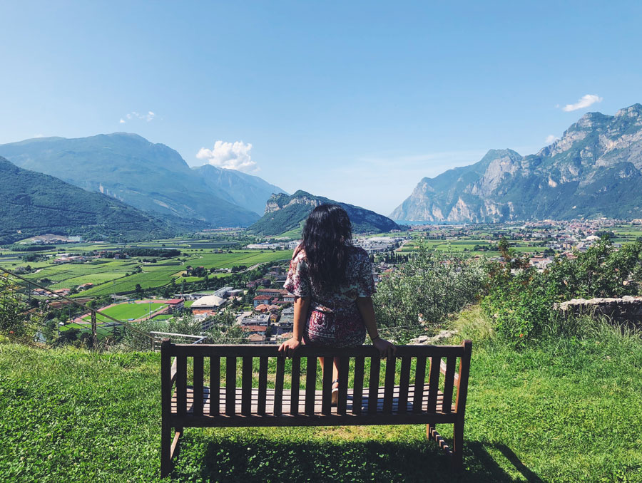 A student sitting on a bench, staring out at a meadow with mountains in the distance.
