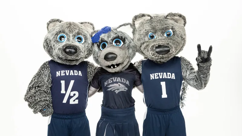The three Nevada mascots, Wolfie Jr., Luna and Alphie, wear Nevada jerseys and stand with their arms around each others back while Alphie makes a wolf sign with his left hand.