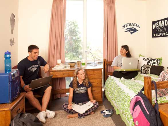 Three students study with notebooks in Sierra Hall at the University of Nevada, Reno, with Nevada logos and posters visible on the walls.