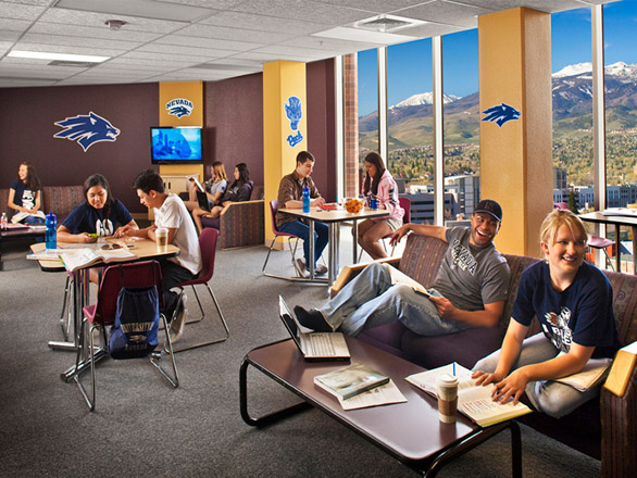 A group of students sit at several tables with notebooks and computers with large bay windows behind them in the Argenta student lounge at the University of Nevada, Reno.