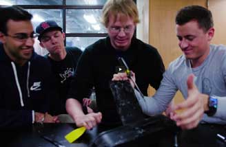 Four engineering students gather around a prototype; one is using a screwdriver