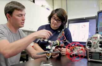 Two engineering sutdents work on a drone, with computers in the background