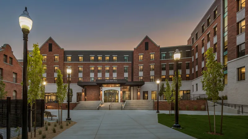 An exterior view of Great Basin Hall, a modern brick residence hall with an illuminated courtyard, lawn areas and walking paths.