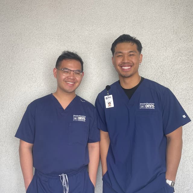 Brothers Lance (left) and Greg (right) Dimapilis wear Orvis School of Nursing blue scrubs and pose for a picture next to each other.