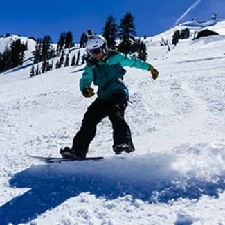 Snowboarder carving through fresh snow down a slope near Lake Tahoe with trees in the background.