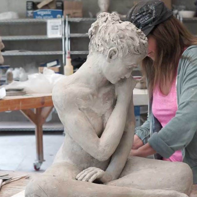 Art studio at the Lake Tahoe campus with a large clay sculpture of a seated figure on a worktable, surrounded by sculpting tools and shelves filled with other clay works in progress.