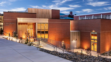 Exterior of the University Arts building, a modern brick building with landscape lighting, large glass doors and windows, grass and landscaping and concrete walkways.