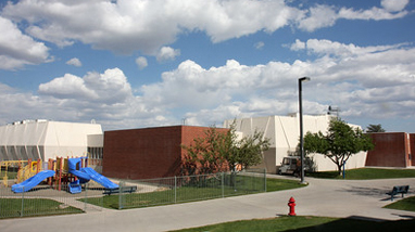 Exterior of Cain Hall, a brick building with white building wings and a playground in front for the CFRC program.