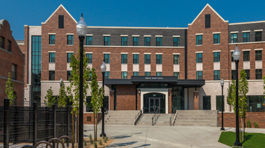 An exterior of Great Basin Hall, a residence hall at the University of Nevada, Reno, a modern brick building with multiple floors, concrete pathways, and trees in front of the building.