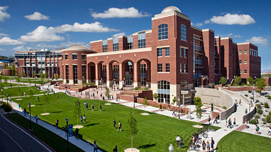 Exterior view of the Mathewson-IGT Knowledge Center, a large modern brick building with numerous windows and a green lawn in front, with students crossing campus in front of the building.