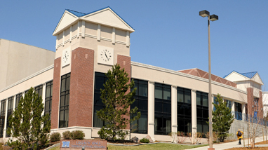 Exterior of Legacy Hall, on the campus of the University of Nevada, Reno, a brick-lined building with large glass windows, a clock, trees and walkways in front of the building.