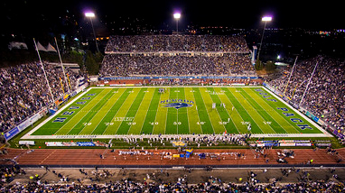 Mackay Stadium, on the campus of the University of Nevada, Reno campus, during an evening football game with thousands of fans in the stands, a green field and the University of Nevada, Reno logo in the middle of the field.