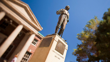 Image of the John Mackay statue on a pedestal standing in front of the Mackay School of Mines, a brick building with large white columns.