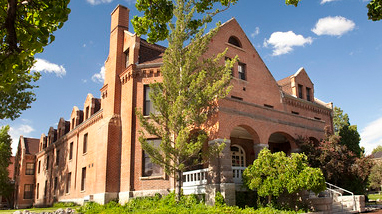 Exterior of Manzanita Hall, an older brick building with large trees and bushes in front of the building.